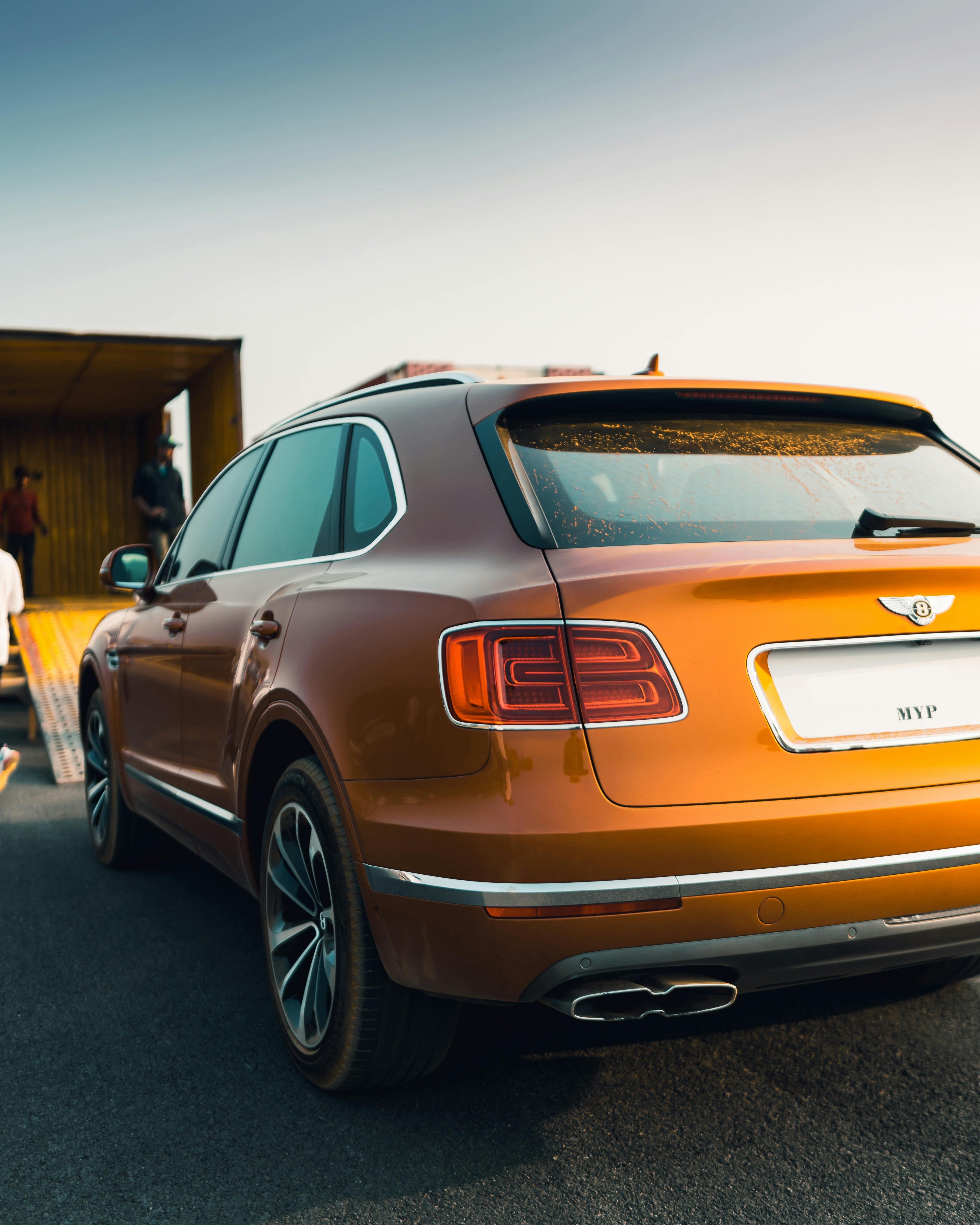 Orange Bentley SUV on a road with people in the background